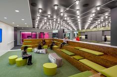 people are sitting on benches in an office lobby with green and yellow seats, while one person sits at the front of the room