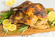 a roasted chicken on a cutting board with lemons and herbs