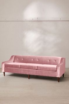 a pink couch sitting on top of a hard wood floor next to a white wall