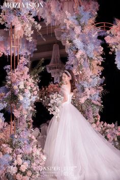 a woman in a wedding dress standing under a floral arch with flowers around her and the words mozzi vision written on it