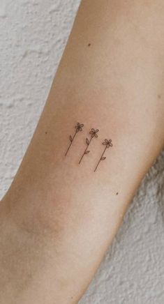 a woman's arm with three small flowers on the back of her left arm