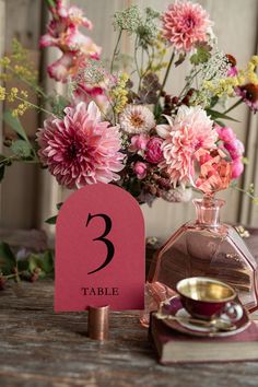 the table numbers are placed next to a vase with flowers in it and a tea cup