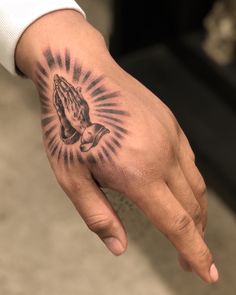 a person's hand with a tattoo that has a praying hand on the palm