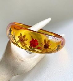 Gorgeous & becoming rare,  Art Deco 1930s reverse carved bakelite bangle In translucent, apple juice Bakelite which is asymmetrical in shape  Reverse carved to the thicker side with flowers & leaves design  looks lovely when it catches the light , almost glows , quite stunning ! Test Positive for Bakelite  bracelet size : Graduating from 1" (2.4 cm)  at widest part  down to 3/8" (0.8cm)  2 & 1/2 " (6.5cm)  internal diameter  In great vintage condition , very light surface wear commensurate  (ver Vintage Resin Bangle, Vintage Lucite Bangle Bracelet, Vintage Yellow Resin Jewelry, Vintage Resin Bracelet, Bakelite Bracelets, Bakelite Jewelry, Bakelite Bangles, Leaves Design, Vintage Bakelite