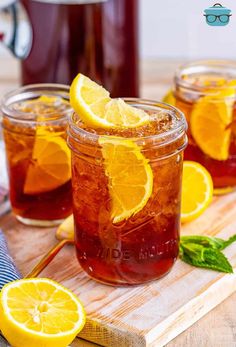 two mason jars filled with iced tea and lemon slices on a cutting board next to a pitcher