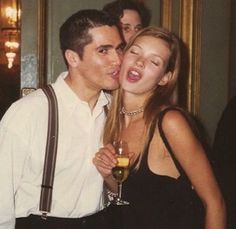 a man kissing a woman while she holds a glass of wine in her hand and smiles at the camera