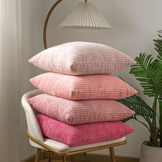 four pillows stacked on top of each other in front of a lamp and potted plant