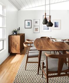 a dining room table with chairs and pictures on the wall above it, along with an area rug