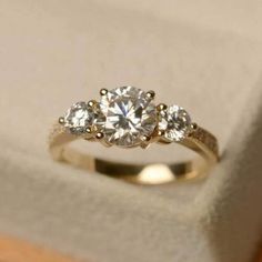 an engagement ring with three stones on it in a box and one is white gold