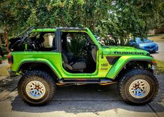 a bright green jeep parked on the side of a road next to trees and bushes