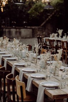 a long table is set with white plates and silverware for an outdoor wedding reception