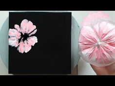 a hand holding a pink flower next to a black box with white and pink flowers on it