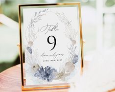 a close up of a table number on a card holder with flowers and seashells