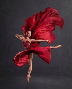 a woman in a red dress is dancing with her arms spread out and she has one leg extended