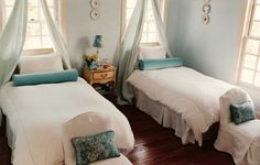 two twin beds in a bedroom with blue walls and white bedding, along with windows