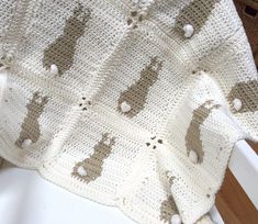 a crocheted blanket with sheeps on it is sitting on a white chair