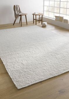 a large white rug in the middle of a room with two chairs and a window