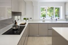 a kitchen with white cabinets and counter tops next to a window that has trees in it