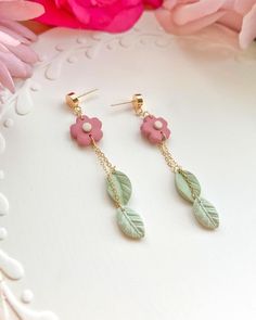 two pairs of earrings with pink flowers and green leaves hanging from them on a white surface