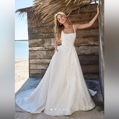 a woman in a white wedding dress standing on the beach next to a straw hut