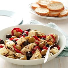 a white bowl filled with olives, red peppers and bread on top of a table