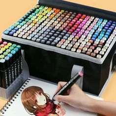 a woman is drawing with colored crayons on the table next to her doll