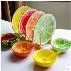 colorful bowls and spoons are arranged on a white table top, with one lemon slice in the middle