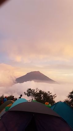 tents are set up in the foreground with a mountain in the distance and clouds below