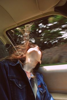 a woman sitting in the back seat of a car with her head out the window