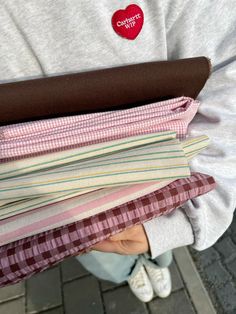 a person holding a stack of folded shirts with a heart patch on the shirt sleeve