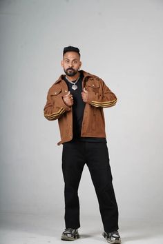 a man standing in front of a white background wearing a brown jacket and black pants