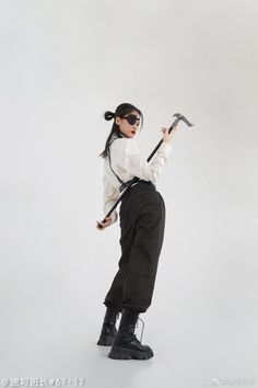 a woman in white shirt and black pants holding an ax with both hands on her hip