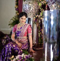 a woman in a purple and pink sari sitting on the ground next to flowers