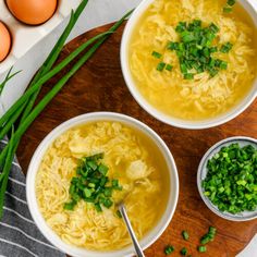 two bowls filled with soup next to eggs and green onions on a wooden cutting board