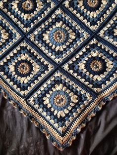 a crocheted blanket on top of a bed covered in black and brown blankets