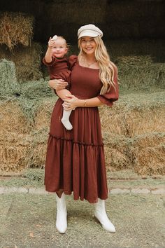 a woman holding a baby in her arms while standing next to some hay bales