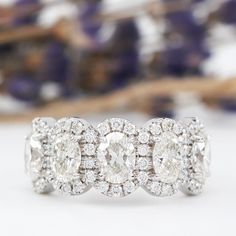 three stone diamond ring on white surface with purple flowers in the backgrouf