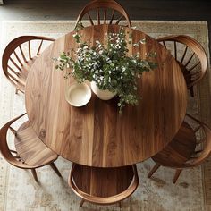 a round wooden table with four chairs around it and a vase filled with flowers on top