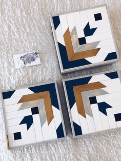 three pieces of wood with geometric designs on them sitting on a white blanket next to an envelope