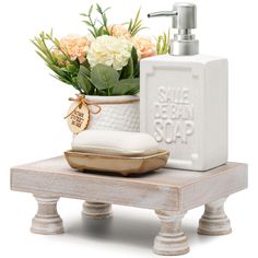 a white soap dispenser sitting on top of a wooden table next to flowers