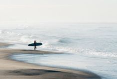 a person holding a surfboard standing on the beach near the ocean with waves coming in