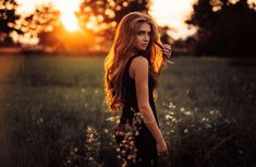 a woman standing in a field at sunset