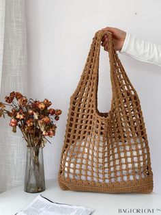 a woman is holding a crocheted bag next to a vase with flowers in it