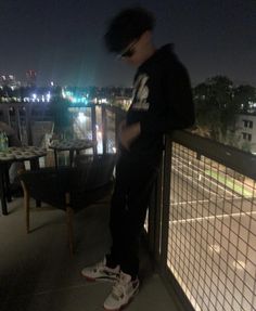 a young man standing on top of a balcony next to a tennis court at night