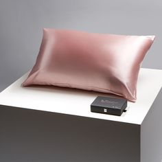 a pink pillow sitting on top of a white table next to a black box and remote control