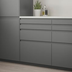 a kitchen with gray cabinets and white counter tops, along with a plant in the corner