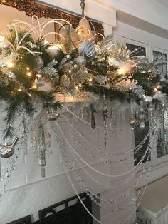 a mantel decorated for christmas with silver and white ornaments, garlands and lights