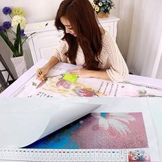 a woman is sitting at a table with paper and scissors in front of her, working on an art project