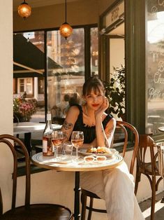 a woman sitting at a table in front of a window with wine glasses on it