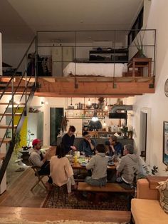 a group of people sitting around in a living room next to a stair case and table